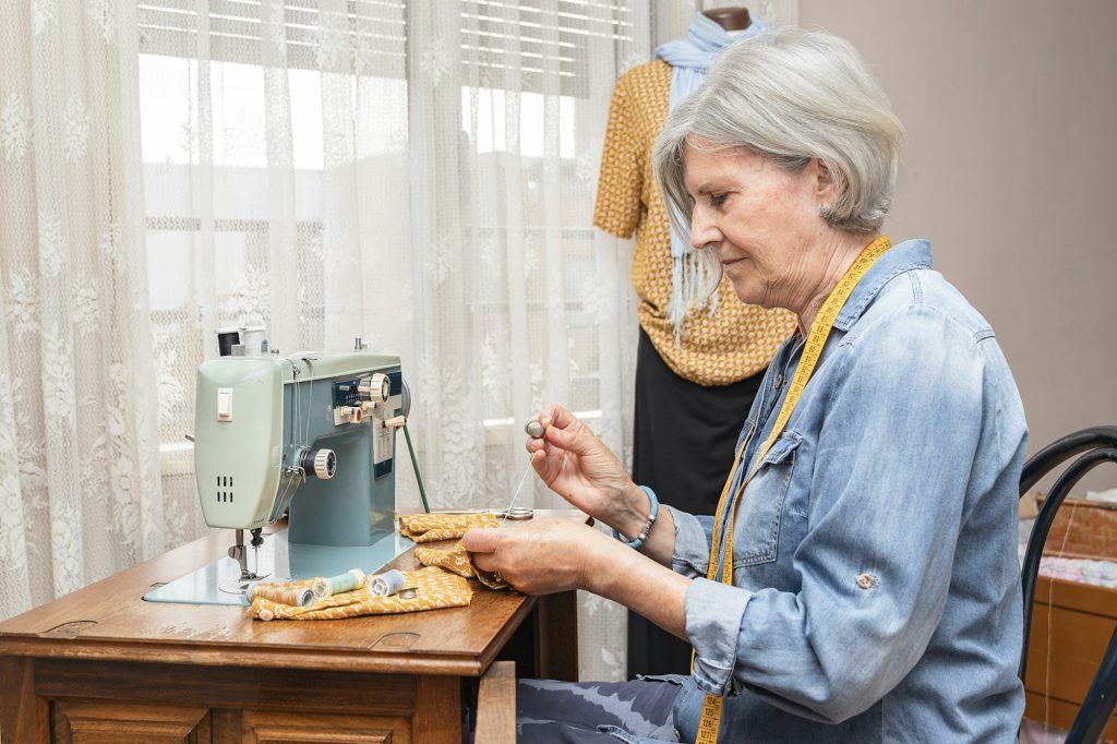 older woman in front of a sewing machine by hand sewing a scrap of orange fabric